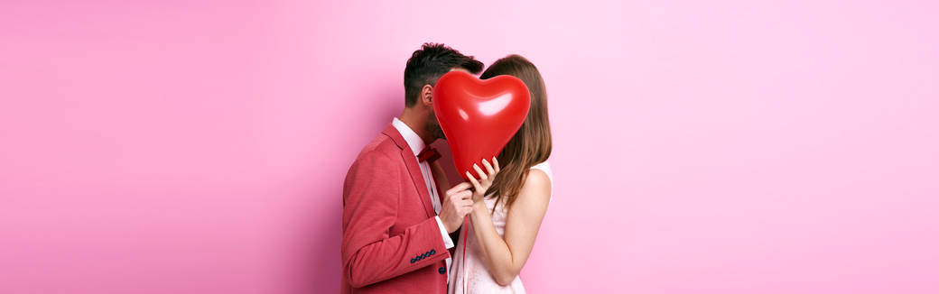couple kissing behind a heart-shaped balloon