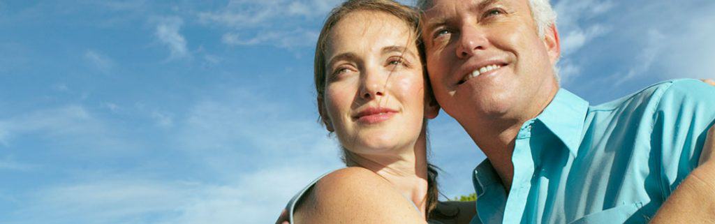 older couple, cheek-to-cheek, smiling while looking into the distance.